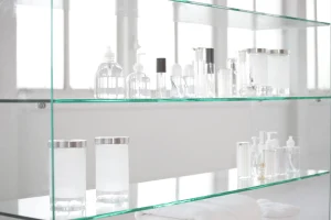 Glasregal nach Maß vom Glaser in einem Badezimmer mit transparenten Kosmetikbehältern, Spenderflaschen und gefalteten weißen Handtüchern.