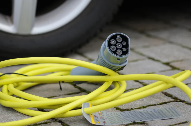 Gelbes Ladekabel für E-Fahrzeuge liegt auf einem gepflasterten Boden vor einem Auto.