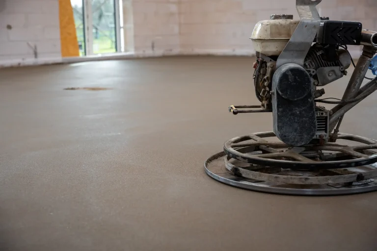 Ein frisch verlegter und geglätteter Estrichboden in einem Rohbau. Im Vordergrund ist eine Schleifmaschine zu sehen, die für die Oberflächenbearbeitung verwendet wird. Die Fläche befindet sich im Zustand vor der CM-Messung zur Bestimmung der Restfeuchte.