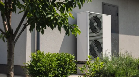 Wärmepumpe vor der grauen Wand eines Familienhaus.