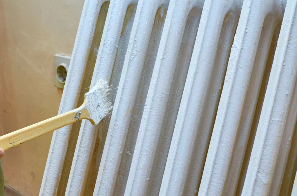 Ein Rippenheizkörper wird mit einem Pinsel weiß frisch gestrichen.
