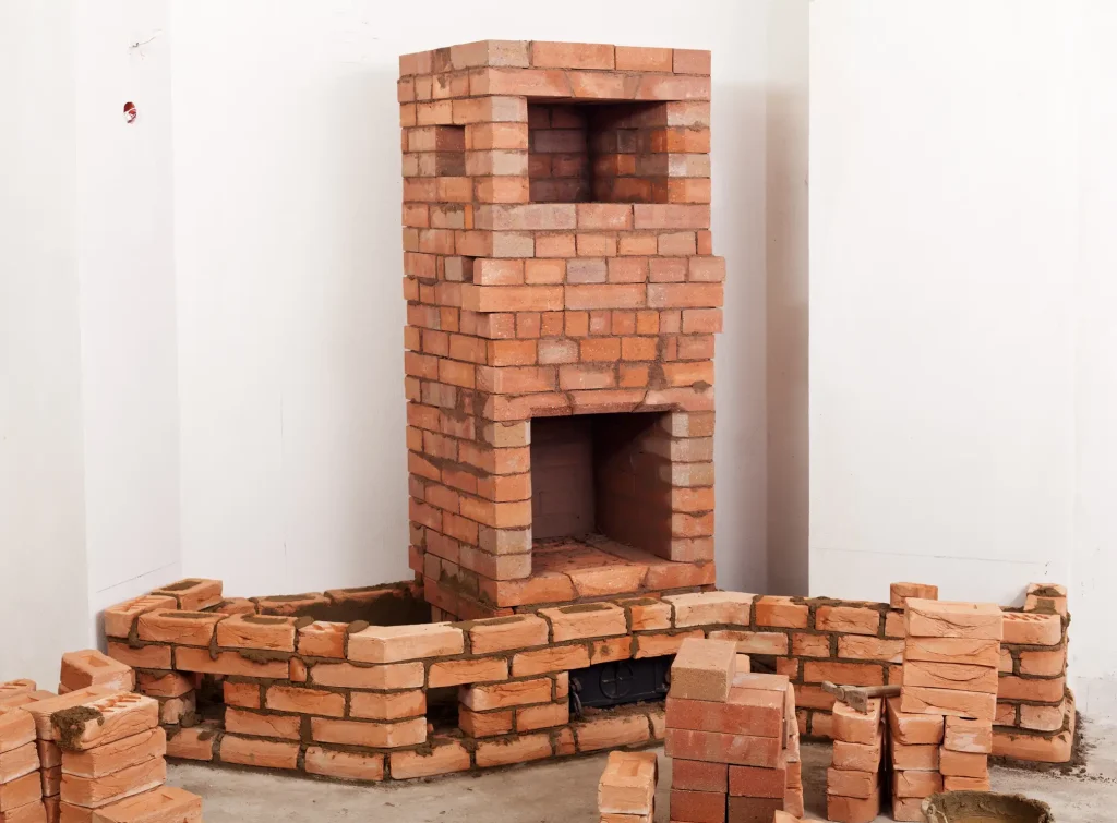 Im Rohbau eines Wohnhauses entsteht ein Kachelofen aus roten Schamottsteinen. Die Ofenanlage befindet sich im Aufbau, mit bereits gemauerter Brennkammer und angedeutetem Zugsystem.