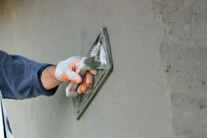 Arbeitskraft trägt mithilfe einer Spachtel Zementputz auf eine Wand auf.