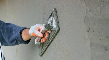 Arbeitskraft trägt mithilfe einer Spachtel Zementputz auf eine Wand auf.