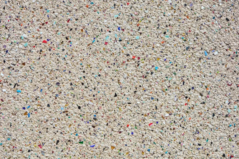 Nahaufnahme einer Fassade mit Buntsteinputz, bestehend aus dicht aneinanderliegenden kleinen Steinchen in den Farben Beige, Rot, Blau und Gelb.