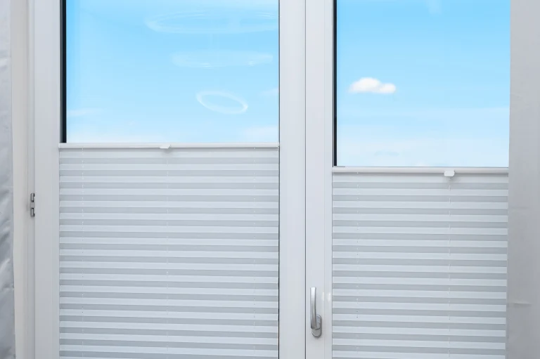 Plisee-Rollos an einem Fenster, welches zu Hälfte geteilt ist. Eine Fensterseite ist gekippt.