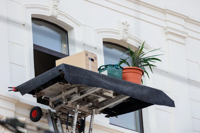 Ein beladener Möbellift während eines Umzugs, vor einem Fenstern im oberen Stockwerk.