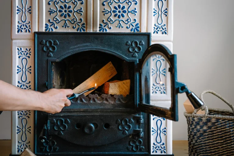 Ein weißer Kachelofen mit blauem Ornamentmuster und einer offenen schwarzen Metalltür, in dem Holzscheite brennen.