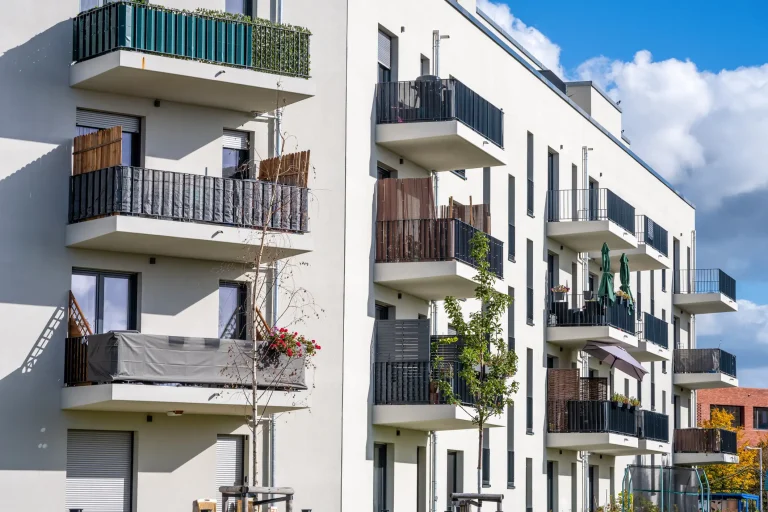 Mehrere übereinanderliegende Kragarmbalkone an einer modernen, hellen Hausfassade mit unterschiedlichen Sichtschutz-Elementen und Geländern.