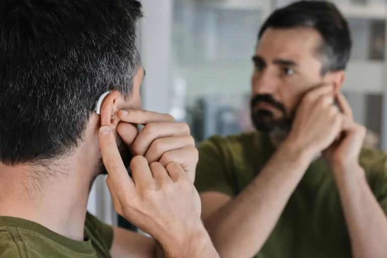 Ein Mann überprüft die Position seines Hörgeräts vor einem Spiegel um eine Rückkopplung zu vermeiden.