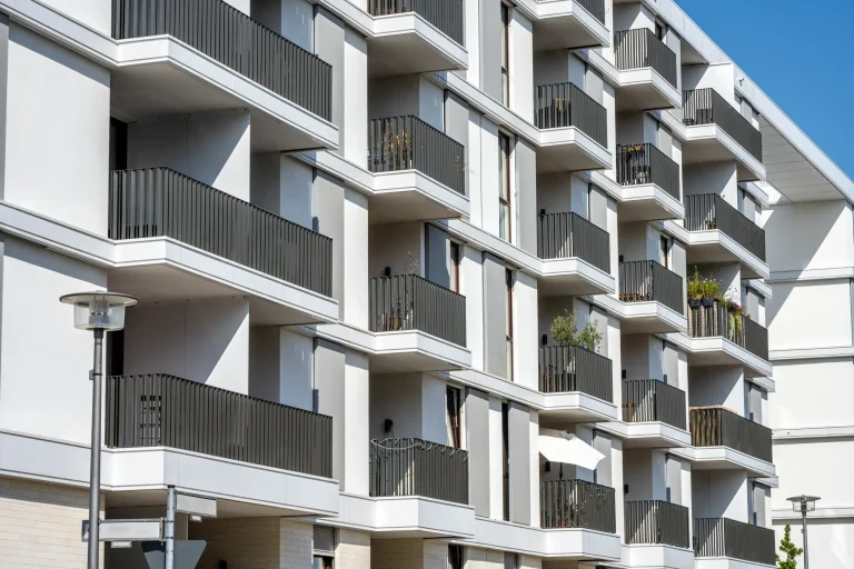 Moderne weiße Wohnanlage mit zahlreichen Balkonen, die mit geradlinigen, dunkelgrauen Aluminium-Balkongeländern in Lamellen-Optik ausgestattet sind.