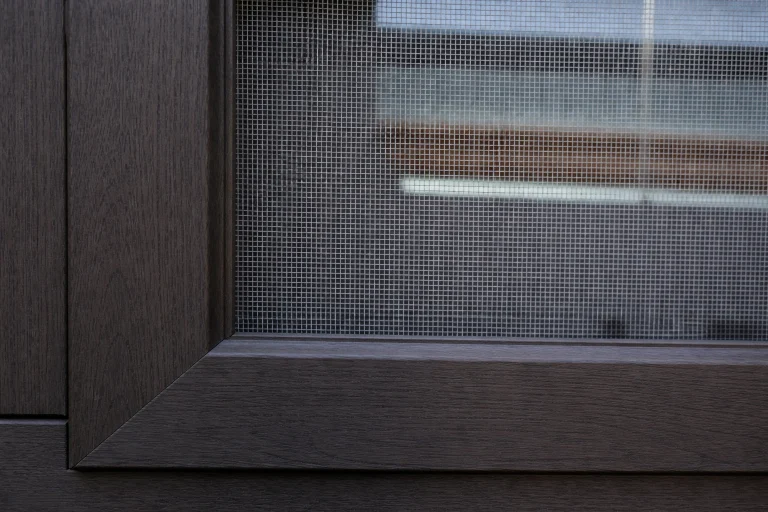 Ein Holzfenster in Nahaufnahme, in welches ein maßgefertigtes Fliegengitter integriert wurde.