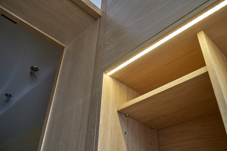 Ein Schrank aus Holz mit leeren Fächern und indirekter Beleuchtung durch einen LED Streifen.