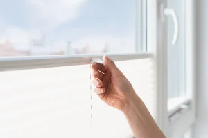 Eine Person schiebt ein Plissee Rollo an einem Fenster nach unten.
