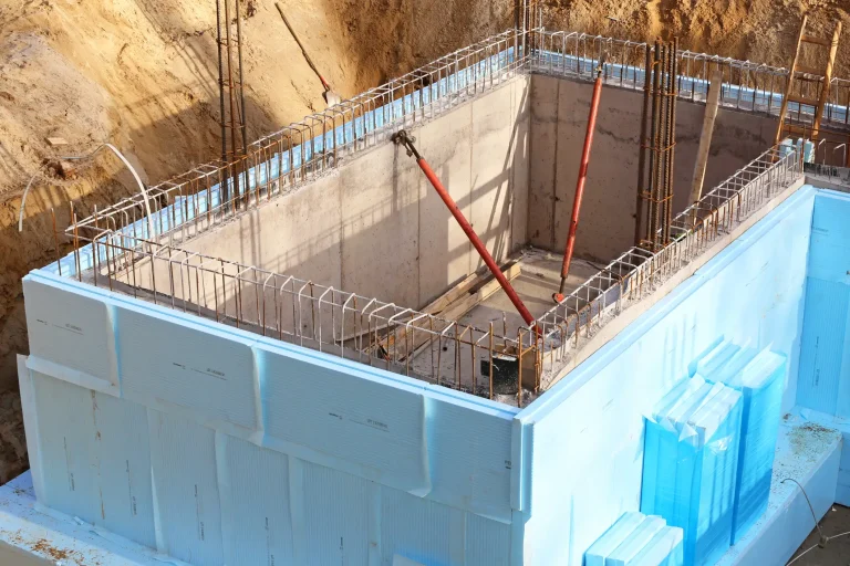 Baustelle eines Hausfundaments mit einer hellblauen XPS-Dämmung an den Außenwänden und einer freiliegenden Bewehrung aus Stahlmatten vor dem Betonieren.