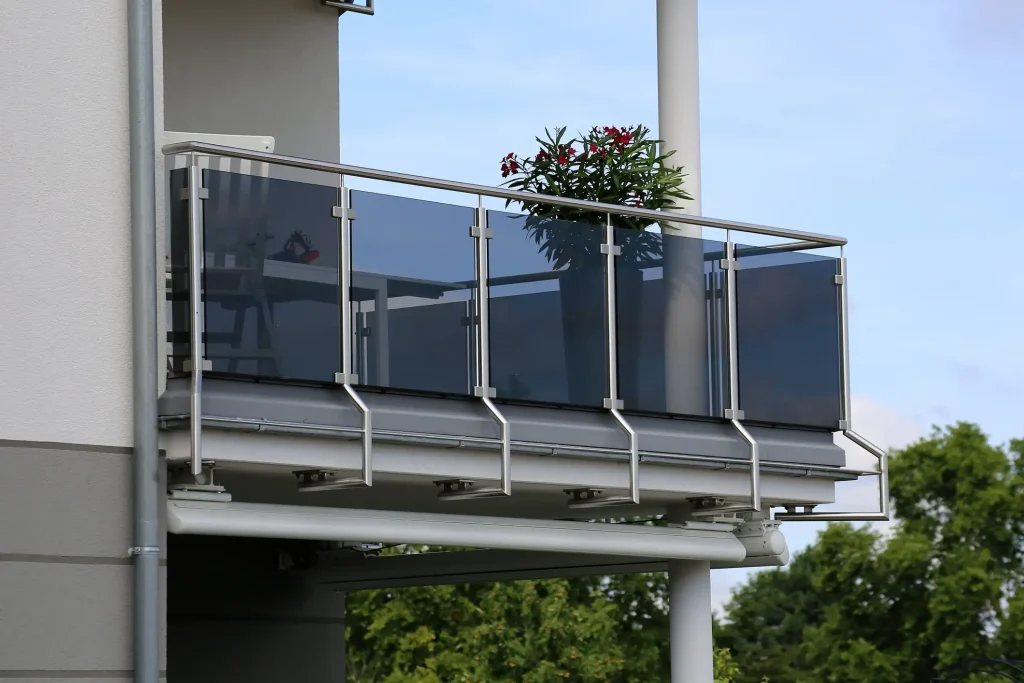 Moderner Balkon mit einer hochwertigen Balkonbrüstung aus glänzendem Edelstahl und getönten Glaselementen. Die Brüstung besteht aus einem Edelstahl-Handlauf und Pfosten, die dunkle Glasfüllungen als Sichtschutz halten.