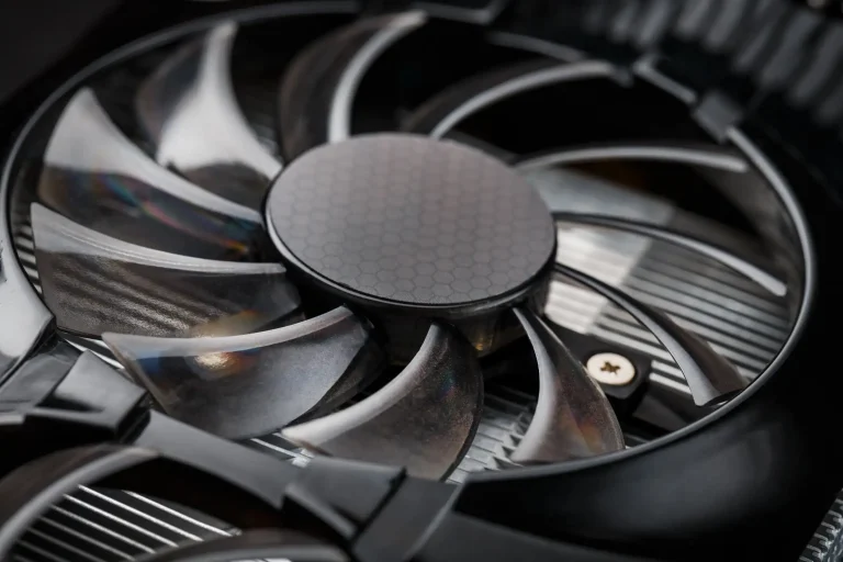 Nahaufnahme eines schwarzen Heizungslüfters mit neun geschwungenen Rotorblättern, der direkt auf den Metall-Lamellen eines Heizkörpers montiert ist, um die Wärmeverteilung im Raum durch Konvektion zu verbessern.