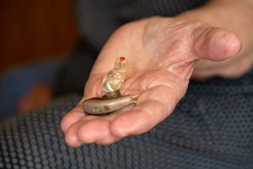 Ein HdO-Hörgerät mit transparentem Ohrpassstück liegt auf der Handfläche einer älteren Person.