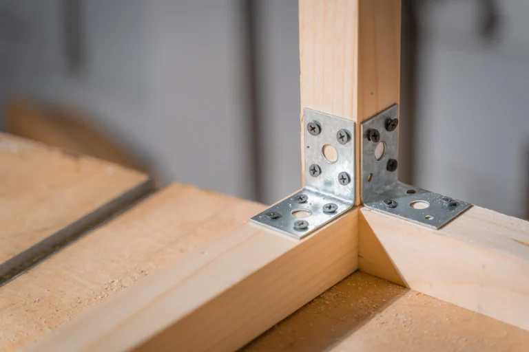 Zwei Edelstahl-Bauverbinder, halten jeweils ein Holzbrett im rechten Winkel fest.