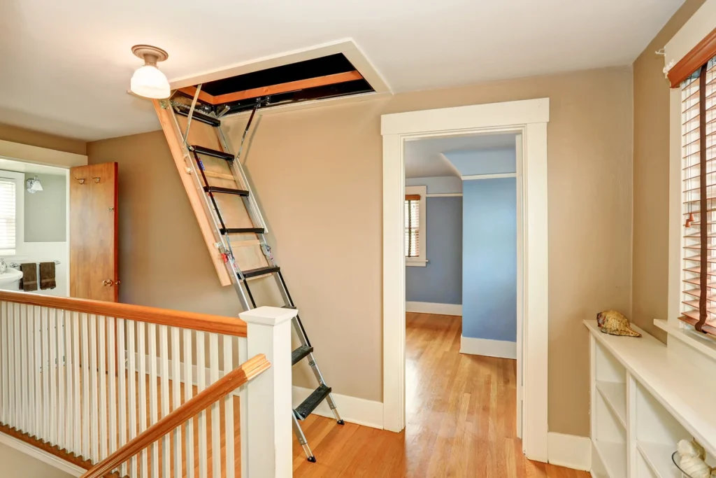 Ausgeklappte Scherentreppe aus Metall als Zugang zum Dachboden in einem Flur.