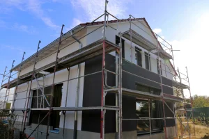 Ein Neubau eines Einfamilienhauses auf einer Baustelle, umstellt von einem Baugerüst. Fertig für eine energetische Sanierung.
