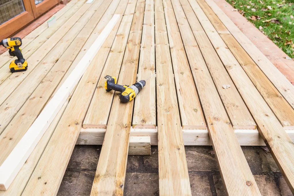 Baustelle einer Holzterrasse aus Kiefernholz während der Montage. Helle, geriffelte Dielen werden auf einer Unterkonstruktion ausgerichtet, während Akku-Bohrschrauber für die Verschraubung auf den Brettern bereitliegen.