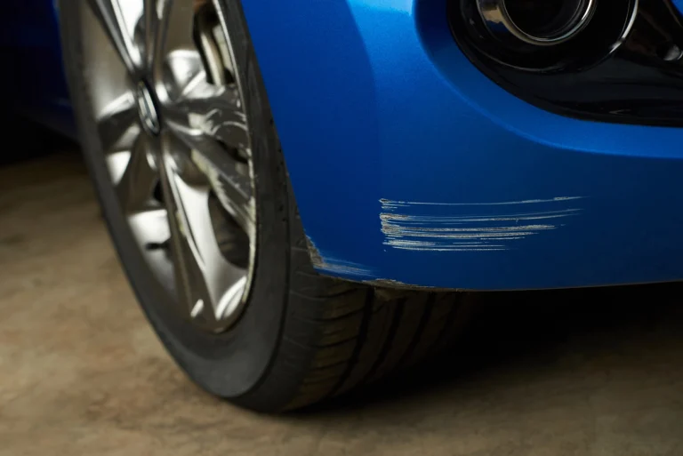 Ein Kratzer in der Stoßstange eines blauen Autos.