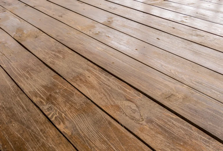 Perspektivische Ansicht einer Terrasse aus Kiefernholz. Die braun lasierten Holzdielen mit sichtbarer Maserung und Astlöchern sind parallel angeordnet und bilden einen strapazierfähigen Bodenbelag für den Außenbereich.