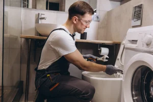 Ein Sanitärinstallateur montiert ein Klo und schließt es an das Rohrsystem, des Hauses an.