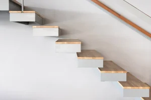 Freischwebende Kragarmtreppe mit Holzstufen an einer weißen Wand.