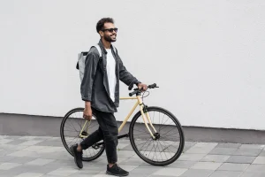 Ein Mann schiebt ein gelbes Fahrrad über einen gepflasterten Gehweg.