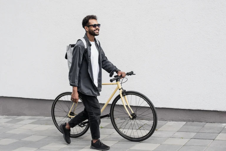 Ein Mann schiebt ein gelbes Fahrrad über einen gepflasterten Gehweg.
