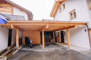 Ein Carport aus Holz. Darunter steht ein Motorrad, geschützt vor Regen.