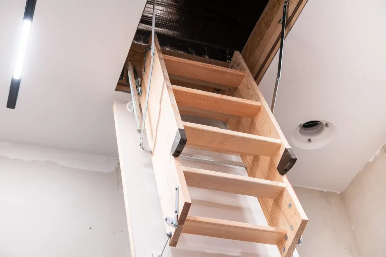 Blick von unten auf eine ausgeklappte, dreiteilige Holztreppe einer Dachbodentreppe (Bodentreppe), die in die geöffnete Deckenluke eines Dachbodens führt.