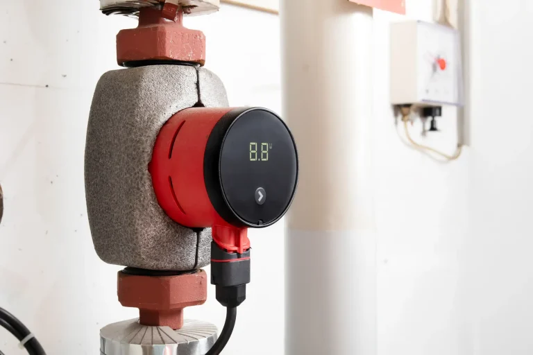 Moderne, rot-schwarze Hocheffizienz-Heizungspumpe mit digitaler Display-Anzeige und Wärmedämmung an einem Heizungsrohr im Heizungskeller.
