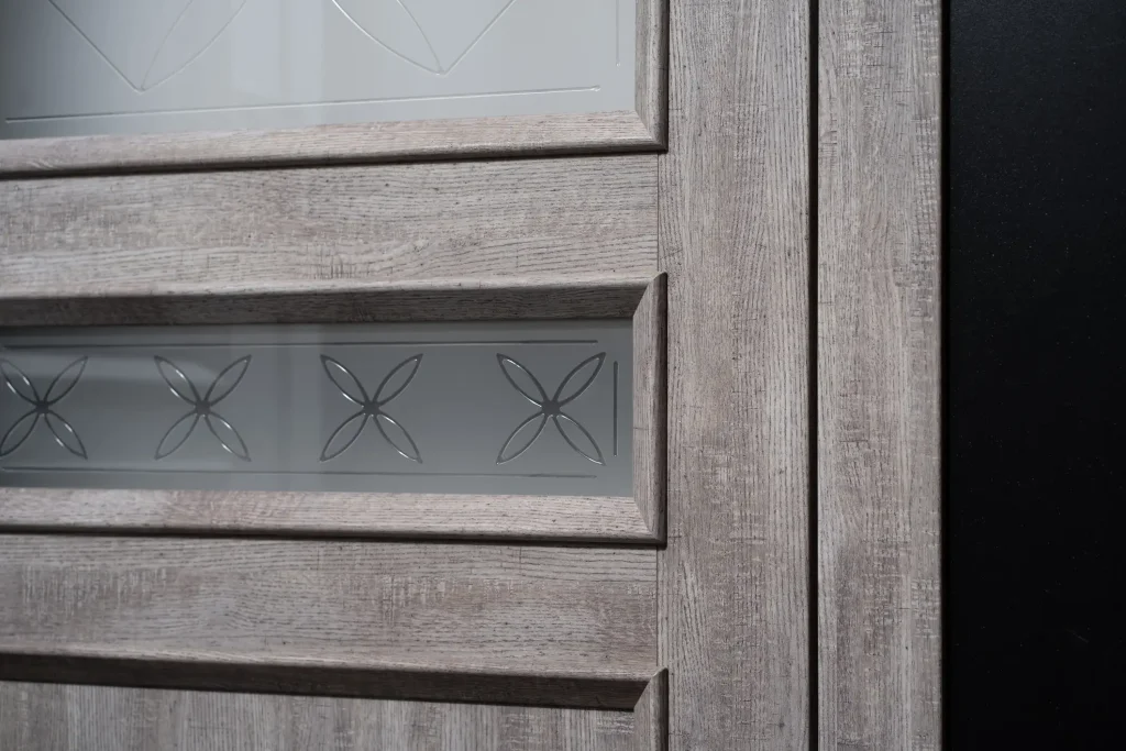 Nahaufnahme einer modernen Zimmertür in grauer Eiche-Optik mit Glasausschnitt. Die Glasscheibe zeigt ein mattiertes Glasdesign mit dezenten, geschliffenen Blumen- oder Rautenmustern.