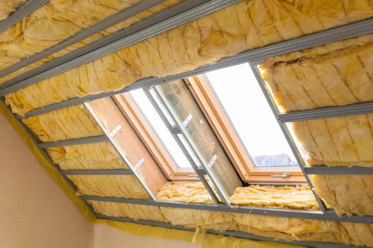 Dachdämmung im Dachgeschoss mit Klemmfilz aus gelber Glaswolle zwischen den Sparren. Eine Metall-Unterkonstruktion für den Trockenbau verläuft quer über die Dämmung rund um zwei große, eingebaute Dachfenster.
