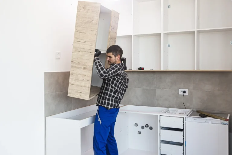 Ein Küchenmonteur hebt einen Oberschrank in Holzoptik an, um ihn an der Wand über den Unterschränken bei einer Küchenmontage zu befestigen.