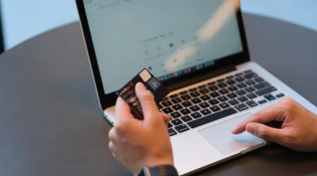 Eine Person hält eine Kreditkarte in der Hand. Sie sitze vor einem Laptop und möchte online etwas bezahlen.
