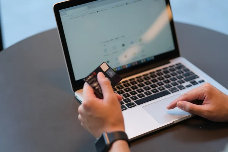 Eine Person hält eine Kreditkarte in der Hand. Sie sitze vor einem Laptop und möchte online etwas bezahlen.