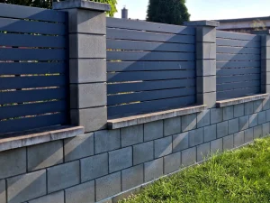 Moderner Sichtschutzzaun aus anthrazitfarbenen horizontalen Lamellen, montiert zwischen massiven grauen Zaunpfosten und einer Sockelmauer aus Betonsteinen.