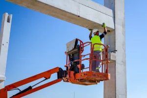 Ein Arbeiter steht auf einer Hubarbeitsbühne und hilft dem Kran beim Ausrichten eines Betonpfostens.