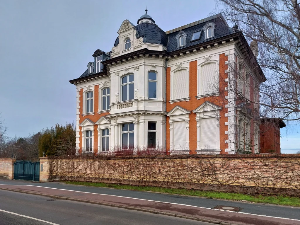 Historische Gründerzeitvilla aus roten Ziegeln mit weißem Fassadenstuck und Mansarddach.
