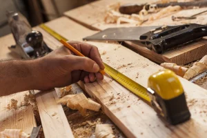 Schreiner misst ein Stück Holz aus und markiert die richtige Stelle mit Bleistift.
