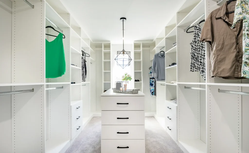 Begehbarer Kleiderschrank nach Maß mit weißen Regalräumen, Kleiderstangen und zentraler Kommode.