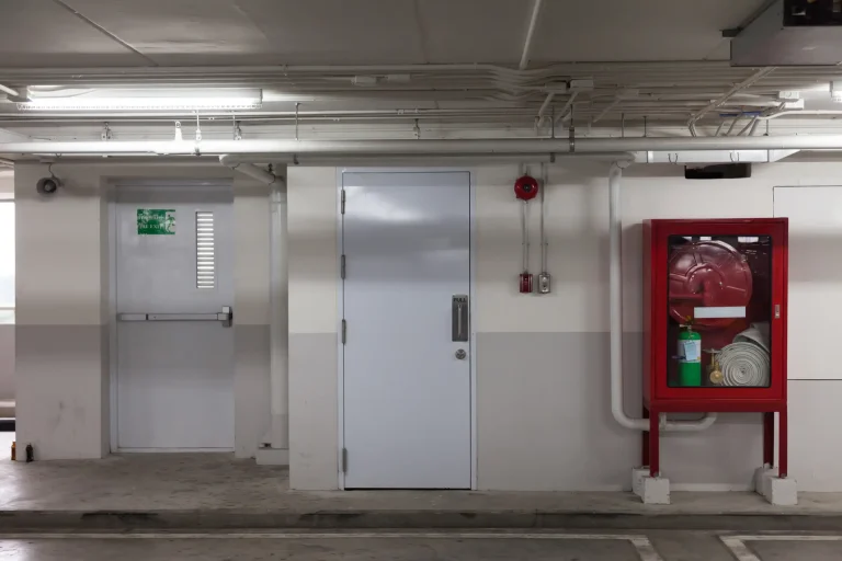 Brandschutztür und Notausgang mit rotem Wandkasten für Feuerwehrschlauch und Feuerlöscher in einem Parkhaus