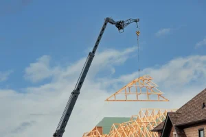 Ein Kran hebt ein neues Holz-Dachbinder-Element zur Dachaufstockung und Anhebung des Dachstuhls auf ein Gebäude.