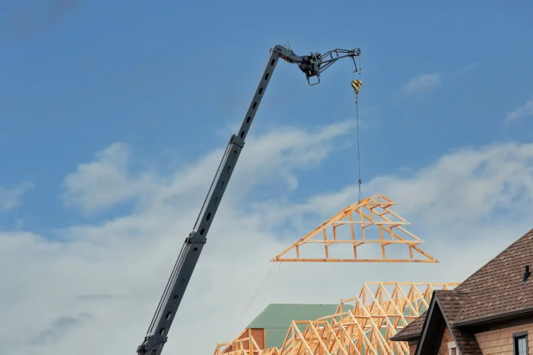 Ein Kran hebt ein neues Holz-Dachbinder-Element zur Dachaufstockung und Anhebung des Dachstuhls auf ein Gebäude.