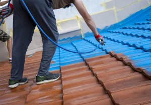 Dachdecker bringt mit einer Spritzpistole eine blaue Dachbeschichtung auf rote Dachziegel auf.