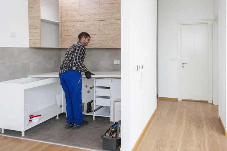Küchenmonteur baut eine moderne Einbauküche mit Holz-Oberschränken auf.